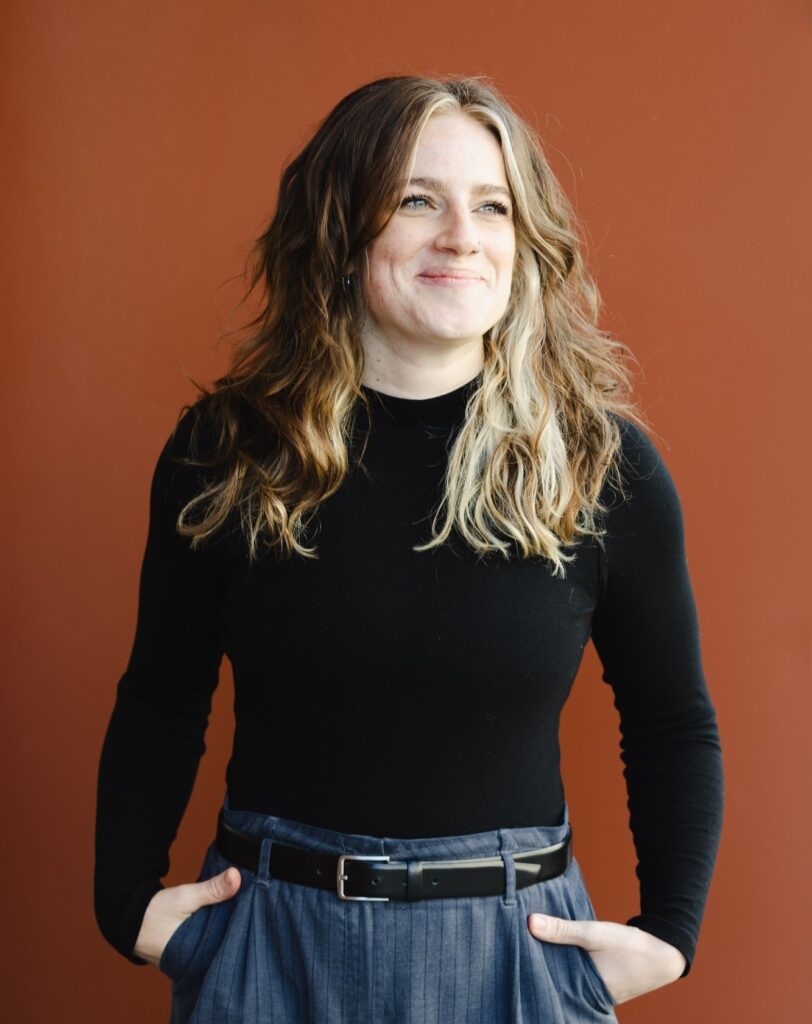 Rebekka schaut rechts an der Kamera vorbei.
Sie lächelt mit geschlossenem Mund.
